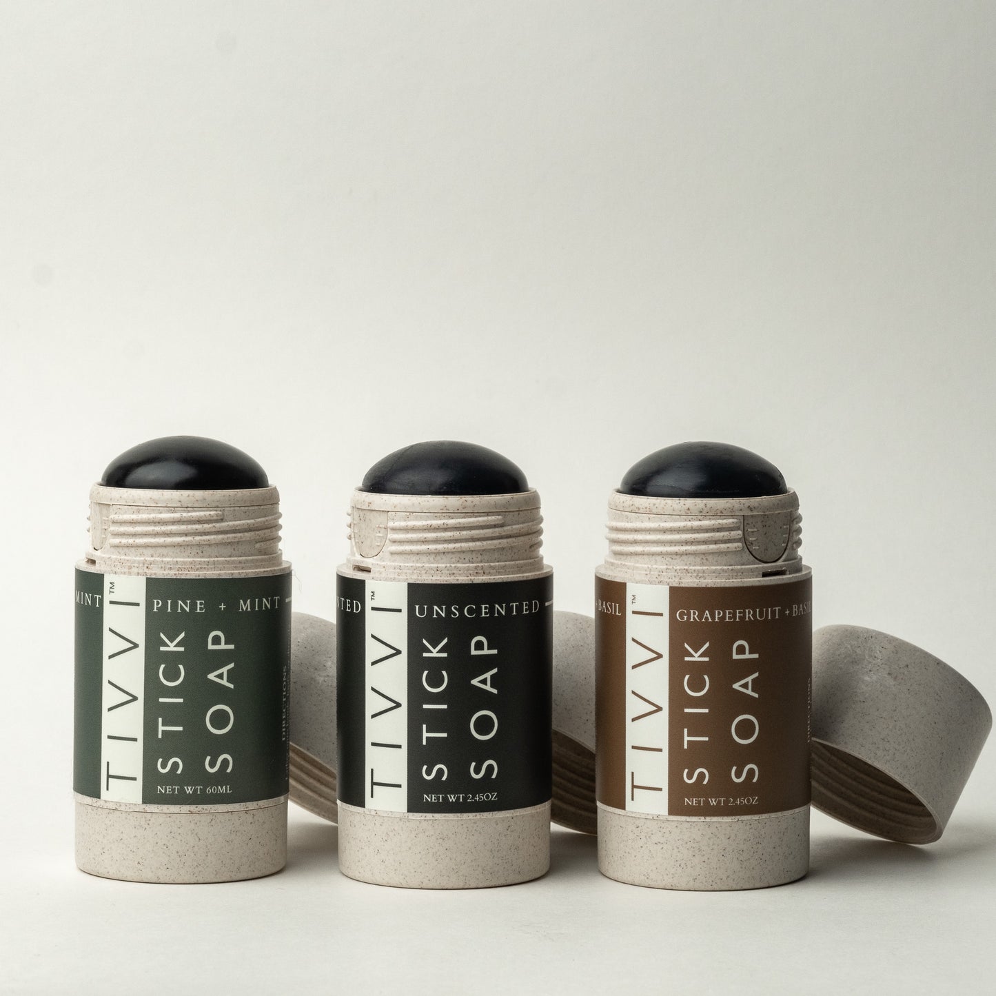 Three sticks from the TIVVI Stick Soap Tri-Pack are displayed against a white background. The varieties shown include Pine + Mint, Unscented, and Grapefruit + Basil. Each soap stick adheres to no animal testing standards, is topped with a black dome, and has a gray, cylindrical base.