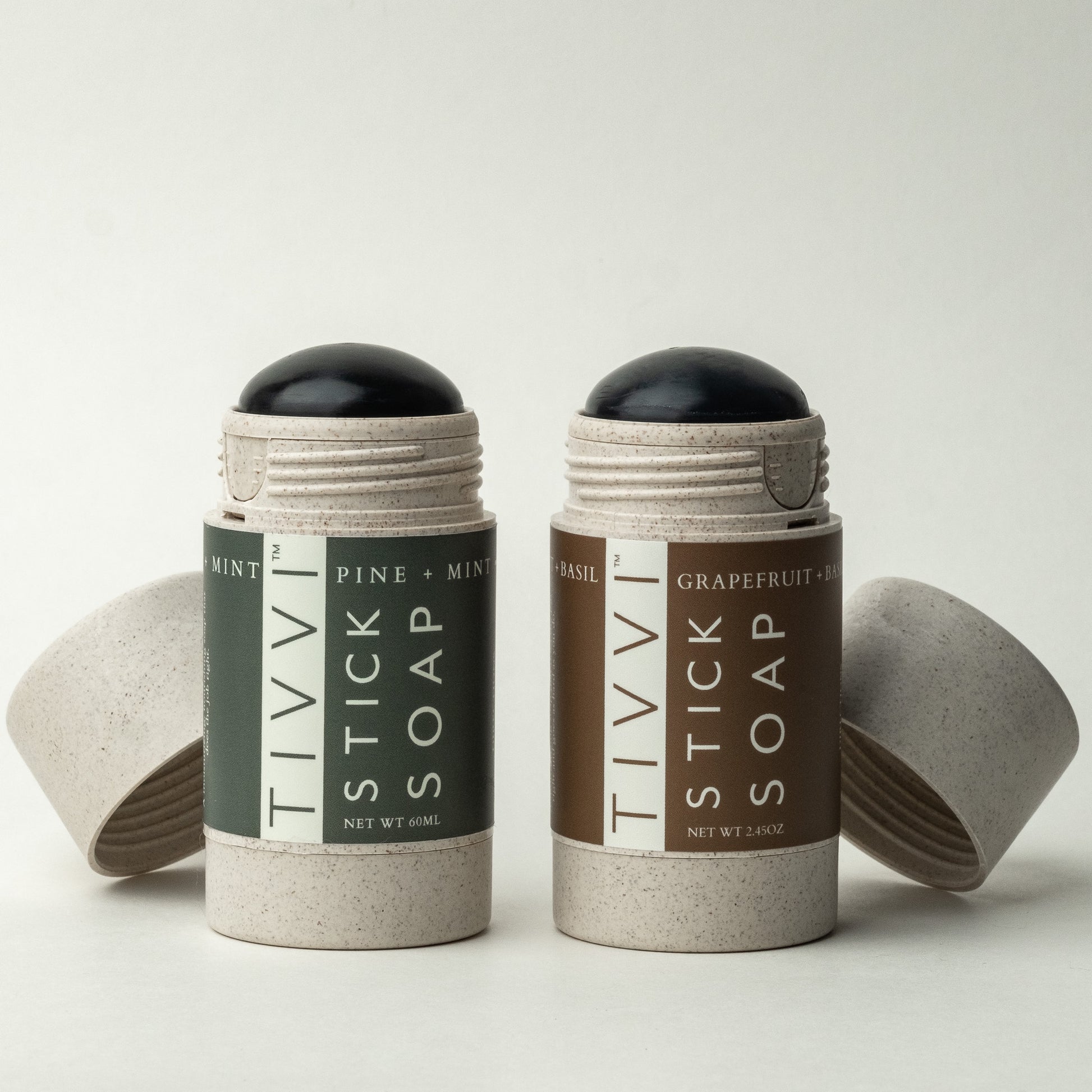 Two cylindrical containers from the Stick Soap Scented Duo-Pack by TIVVI are displayed against a neutral background. The left container, labeled "Mint Pine + Mint" in green, sits next to the right container labeled "Basil Grapefruit + Basil" in brown. Both containers have their caps removed, showcasing the vegan soap inside.